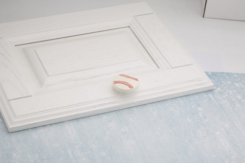 Gałka meblowa w kształcie piłki do baseballu zamontowana na białym froncie szuflady